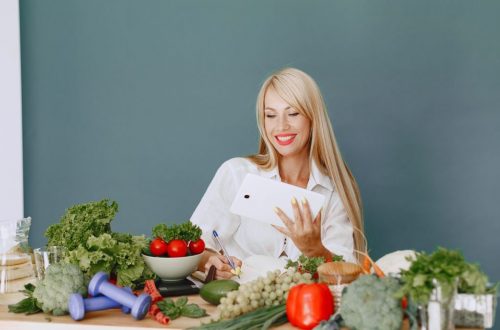 Woman using a tablet surrounded by fresh vegetables at a table, showcasing healthy lifestyle and technology.